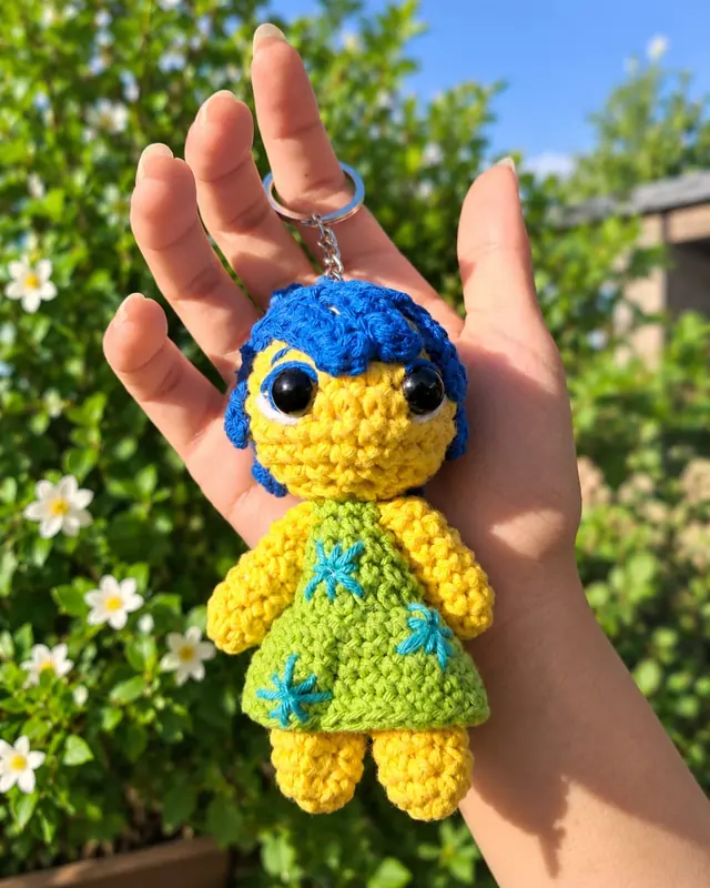 Llavero amigurumi de personaje amarillo con pelo azul y vestido verde