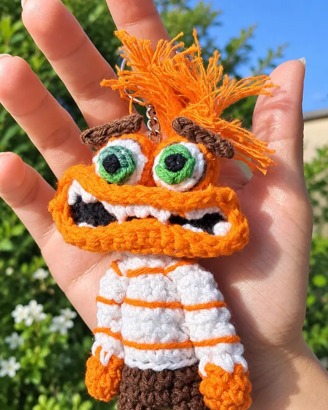 Llavero amigurumi de personaje naranja con pelo revuelto y buzo rayado