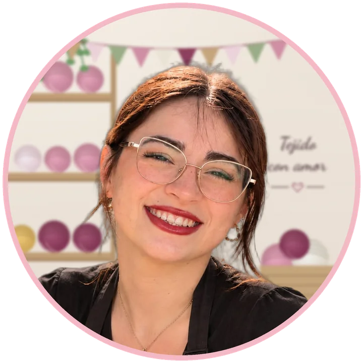 Foto de Jocelyn, la tejedora de Al Punto Paz, sonriendo en su taller, con estantes de ovillos y banderines tejidos
